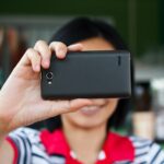 Ręki dotyka smartphone jaskrawego tło, zbliżenie
