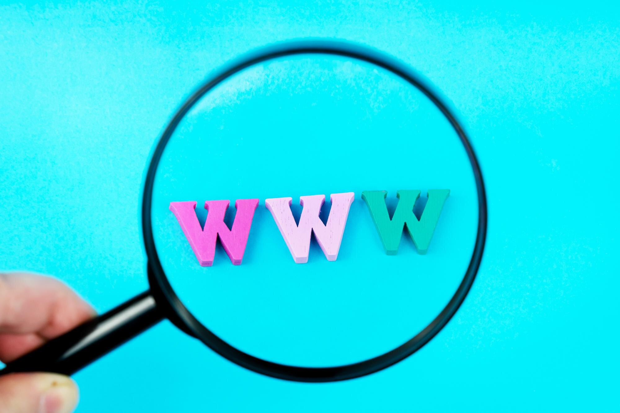 Wielokolorowe drewniane litery WWW pod lupą na jasnoniebieskim tle. Symbol Internetu World Wide Web. Kreatywna koncepcja biznesu online, rozpowszechnianie informacji przez Internet.