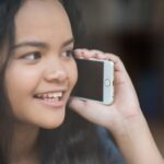 Młoda kobieta korzystająca i patrząca na smartfon z poczuciem szczęścia