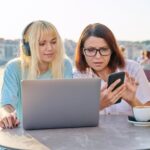 Poważna matka i nastoletnia córka razem w kawiarni na świeżym powietrzu, patrząc na laptopa