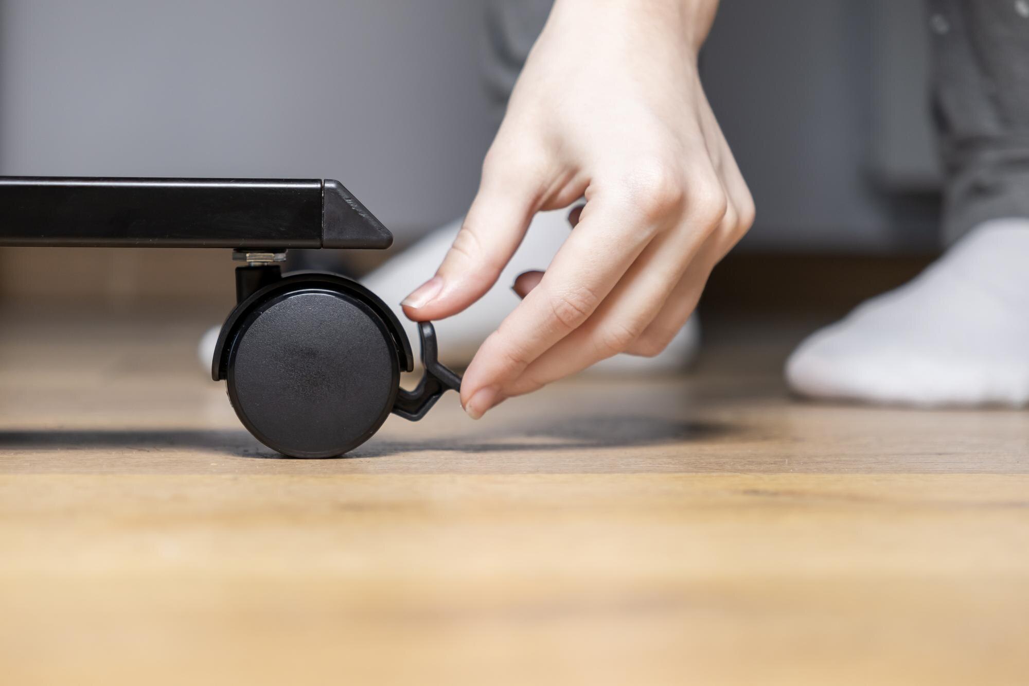 Person39s hand engaging the brake on a black caster wheel of modern furniture ensuring stability and safety for mobility in a contemporary home setting