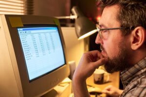 Caucasian man analyzing spreadsheet data on desktop computer screen